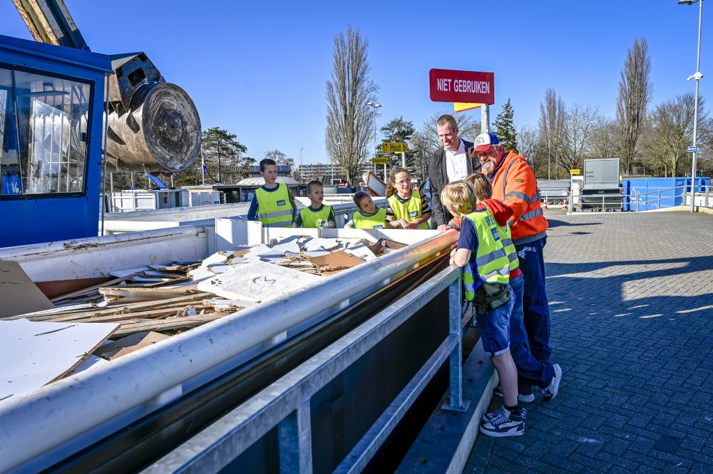 Wethouder Geissler en de kinderen krijgen uitleg van een medewerker van de milieustraat bij een container.