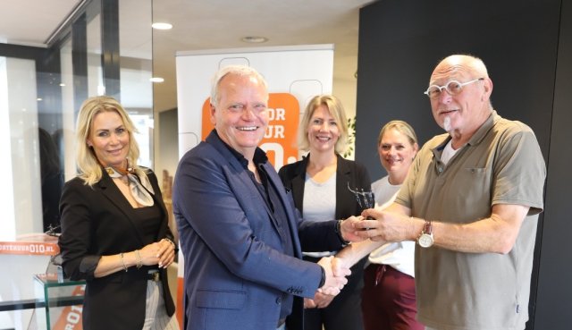 Wethouder Eric Faasssen overhandigt het beeldje aan Wim Schipper, met zijn dochters op de achtergrond
