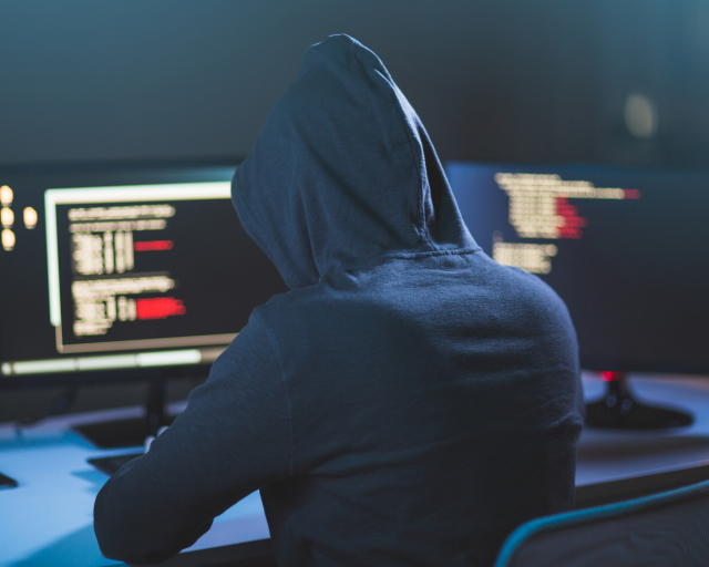 Een persoon in een hoodie achter twee computerschermen