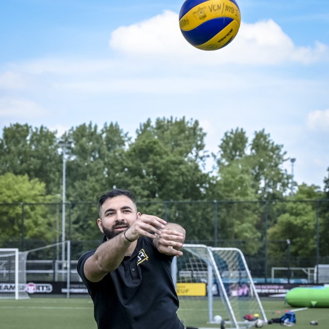 Een lid van de Capelse Jongerenraad gooit een volleybal omhoog op een sportveld tijdens de sportdag