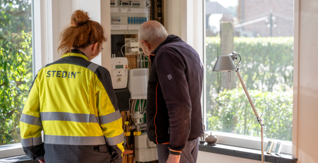 Een oudere man en een medewerker van Stedin kijken samen in de meterkast.