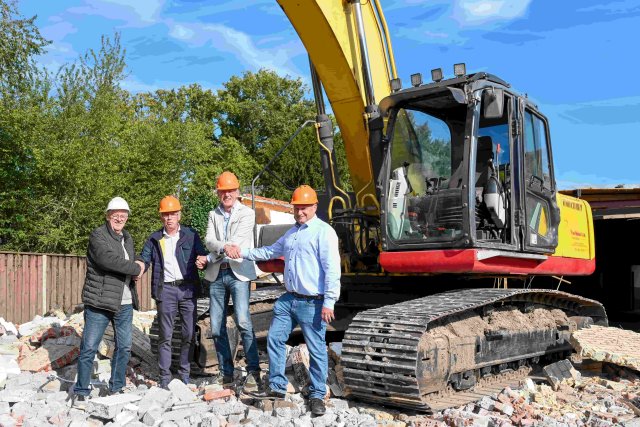 Foto van een graafmachine en vier mensen die elkaar een handgeven