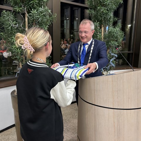 Burgemeester Michael Sijbom geeft kinderburgemeester Milou Groen een ingepakt cadeau.