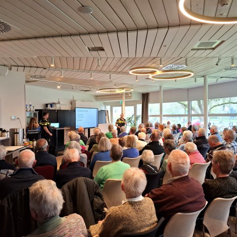 Op de foto een zaal vol mensen die kijken naar de presentatie van een politieagent tijdens de voorlichtingsbijeenkomst op 2 april 2026