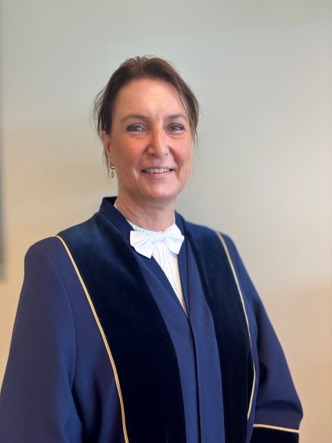 Irene Nuiten-Lugtenberg kijkt lachend naar de camera gekleed in een blauwe toga