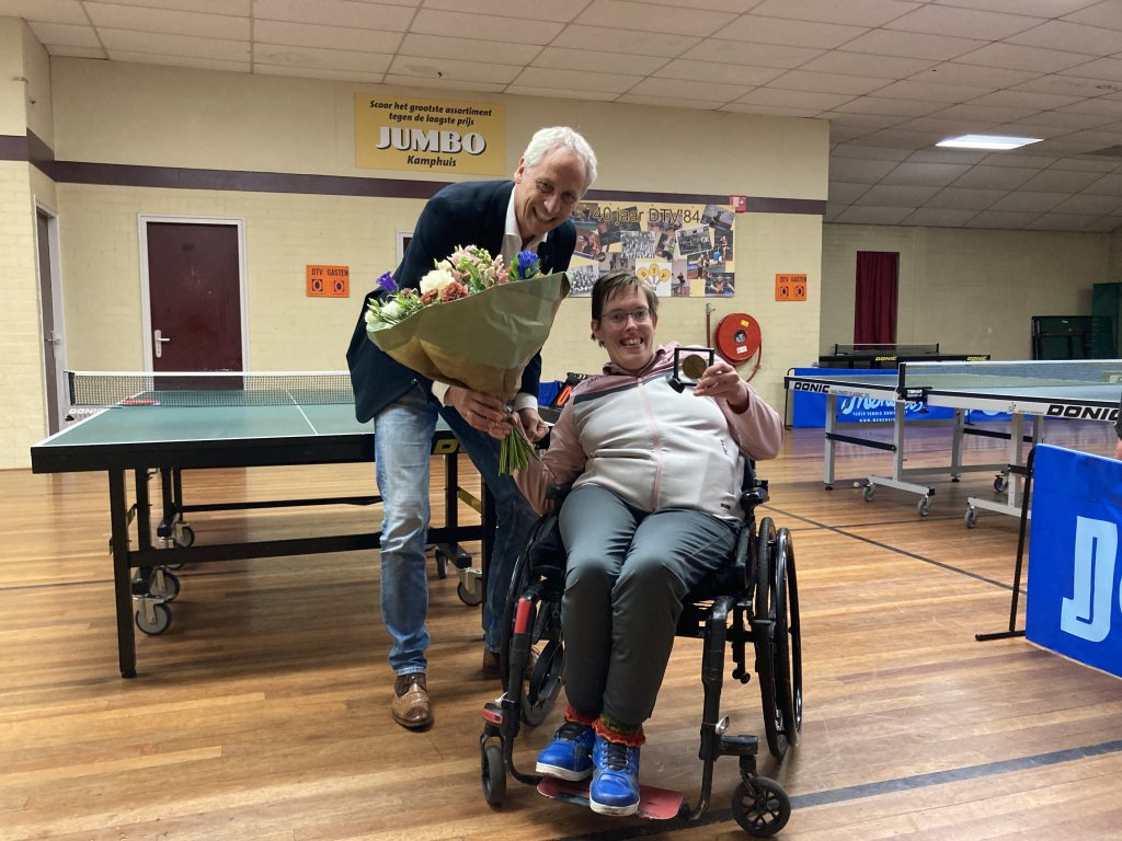 Op de foto staan wethouder Jan Uitslag en Mariëlle Boers. Mariëlle zit in een rolstoel en ze houdt haar net ontvangen sportpenning vast.