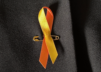 Op de foto is een oranje lintje opgespeld op een kledingstuk in het kader van de Wereld Suïcide Preventie Week