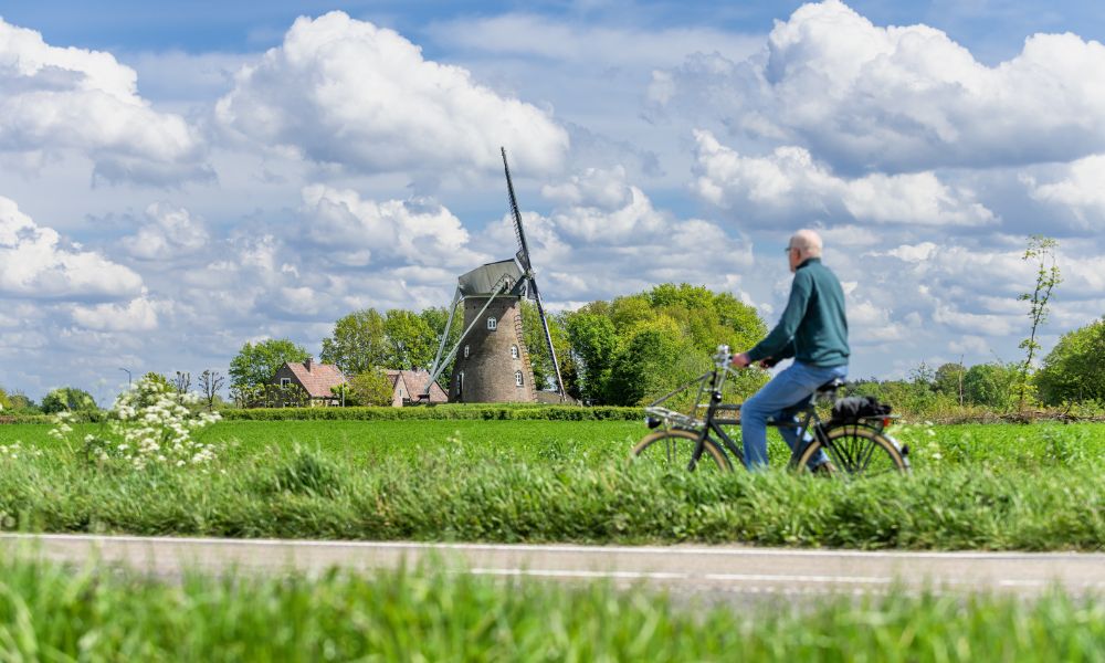 Foto van een fietser met op de achtergrond molen Johanna Elisabeth in Vlierden