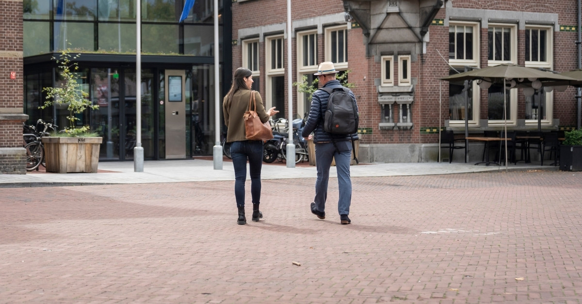 Twee personen lopen richting de hoofdingang van het Huis voor de samenleving.
