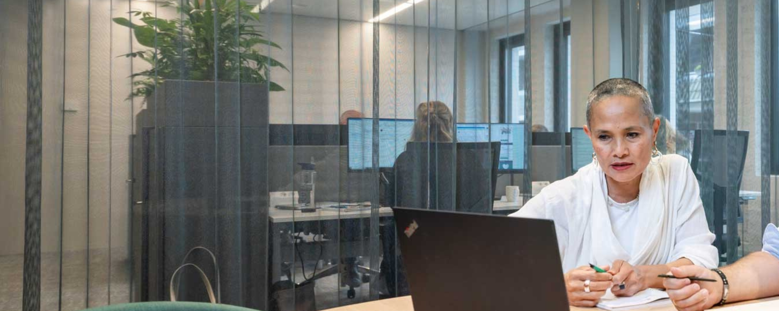 Medewerkers zitten in een vergadering te overleggen en aantekeningen te maken, kijkend naar het scherm van de laptop.