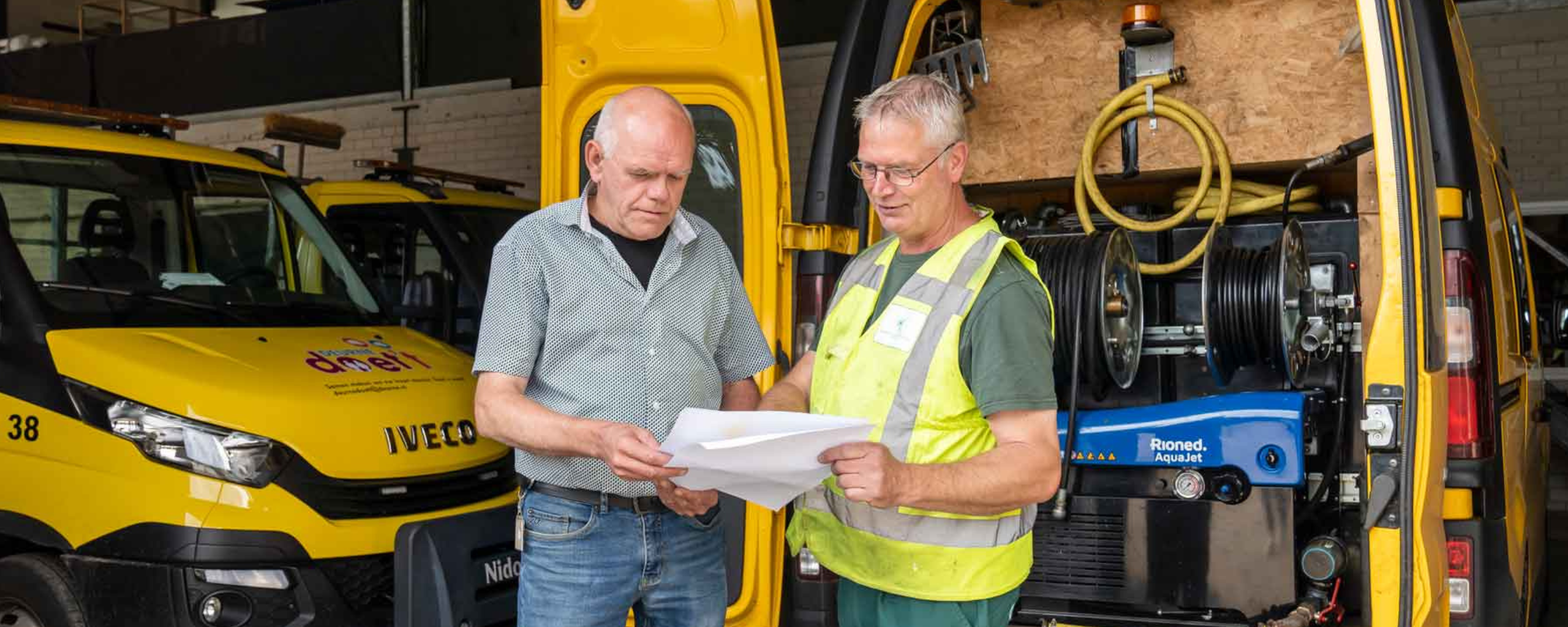 Twee buitendienst medewerkers bespreken samen wat er op het papier geschreven of afgebeeld staat.