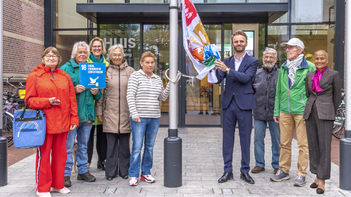 Wethouder Tom Oomen hijst samen met Platform Global Goals Deurne, stagiaire Karin (via Peelprokkelstage) en andere betrokkenen de Global Goals-vlag voor het Huis van de samenleving in Deurne.