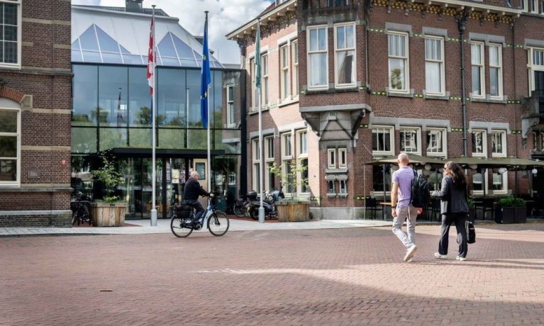 Twee medewerkers lopen over het plein richting het Huis voor de samenleving.