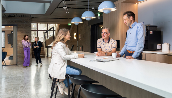 Collega’s zijn met elkaar zowel staand als zittend in gesprek in de ontmoetingsruimte in het Huis voor de samenleving.