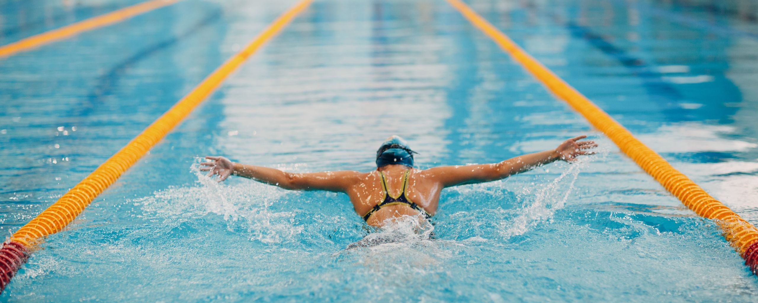 Een vrouwelijk persoon die aan het zwemmen is, ze doet de vlinderslag.