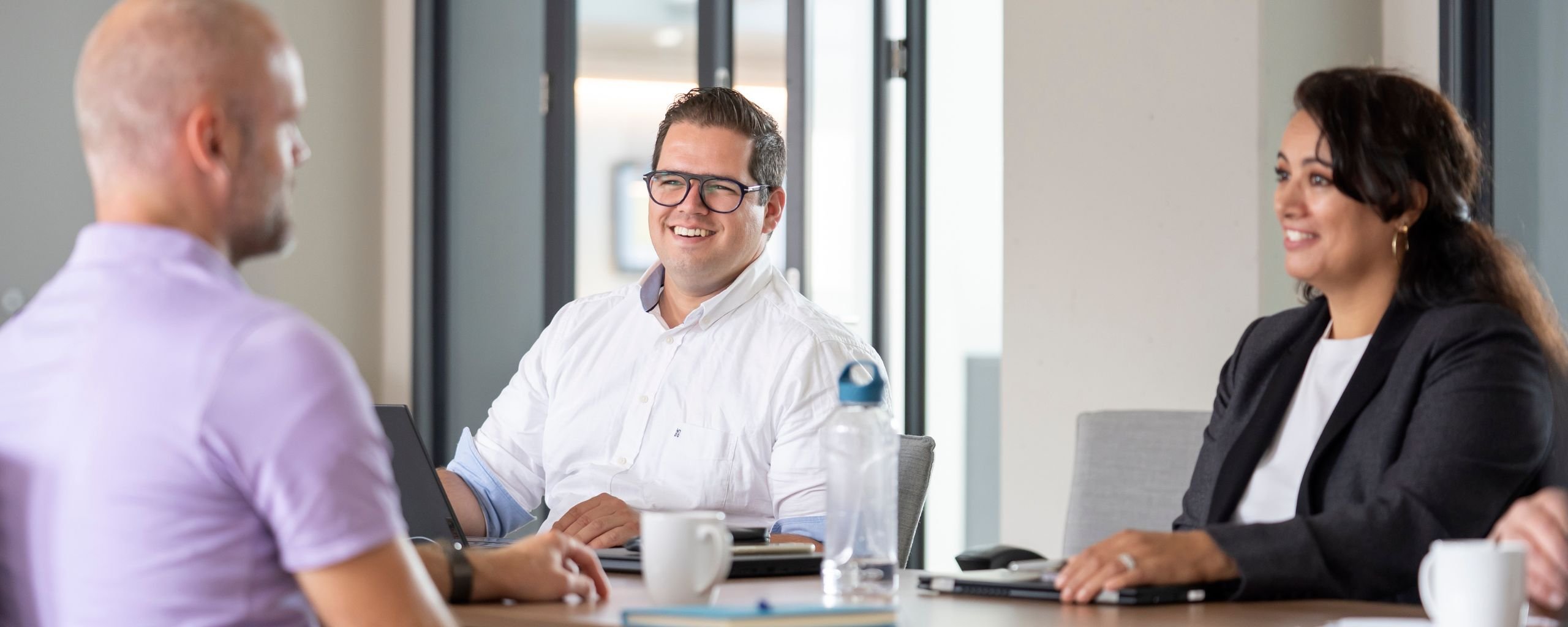 Drie medewerkers zitten samen in een overleg in een vergaderruimte.
