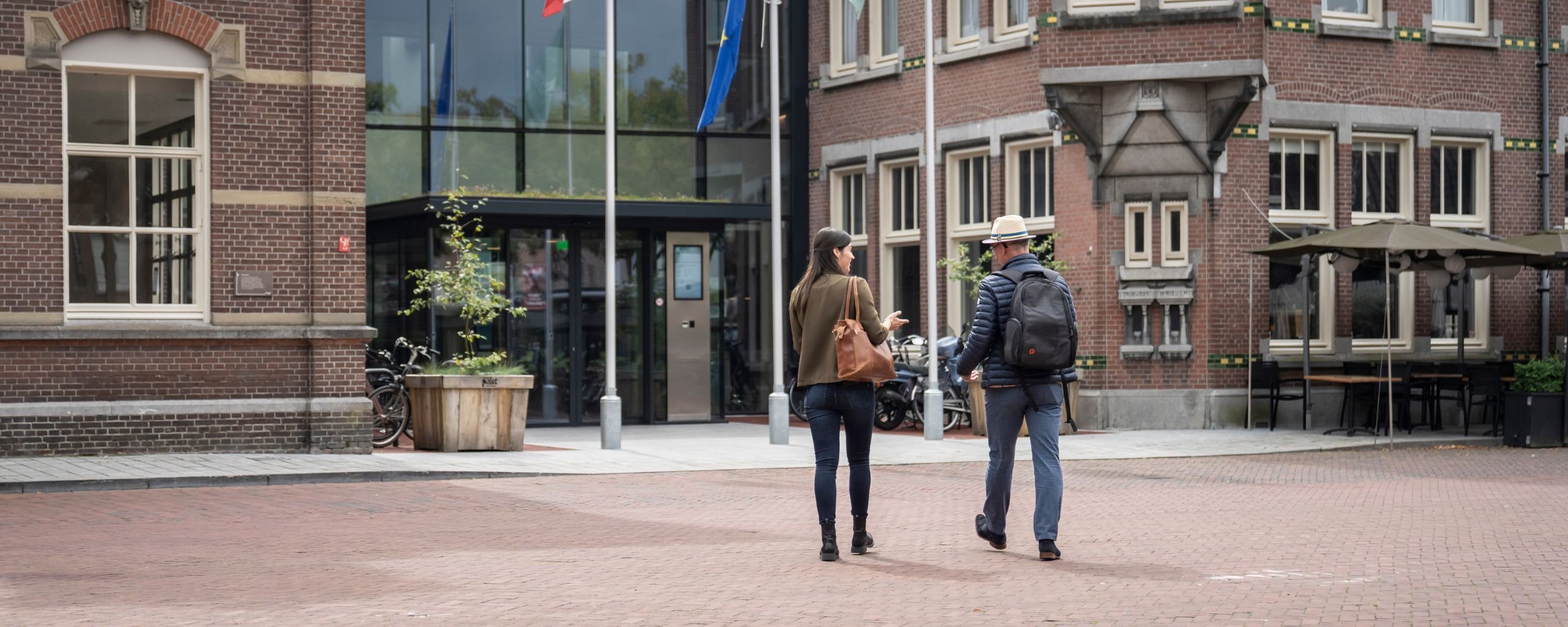 Twee personen lopen richting de hoofdingang van het Huis voor de samenleving.