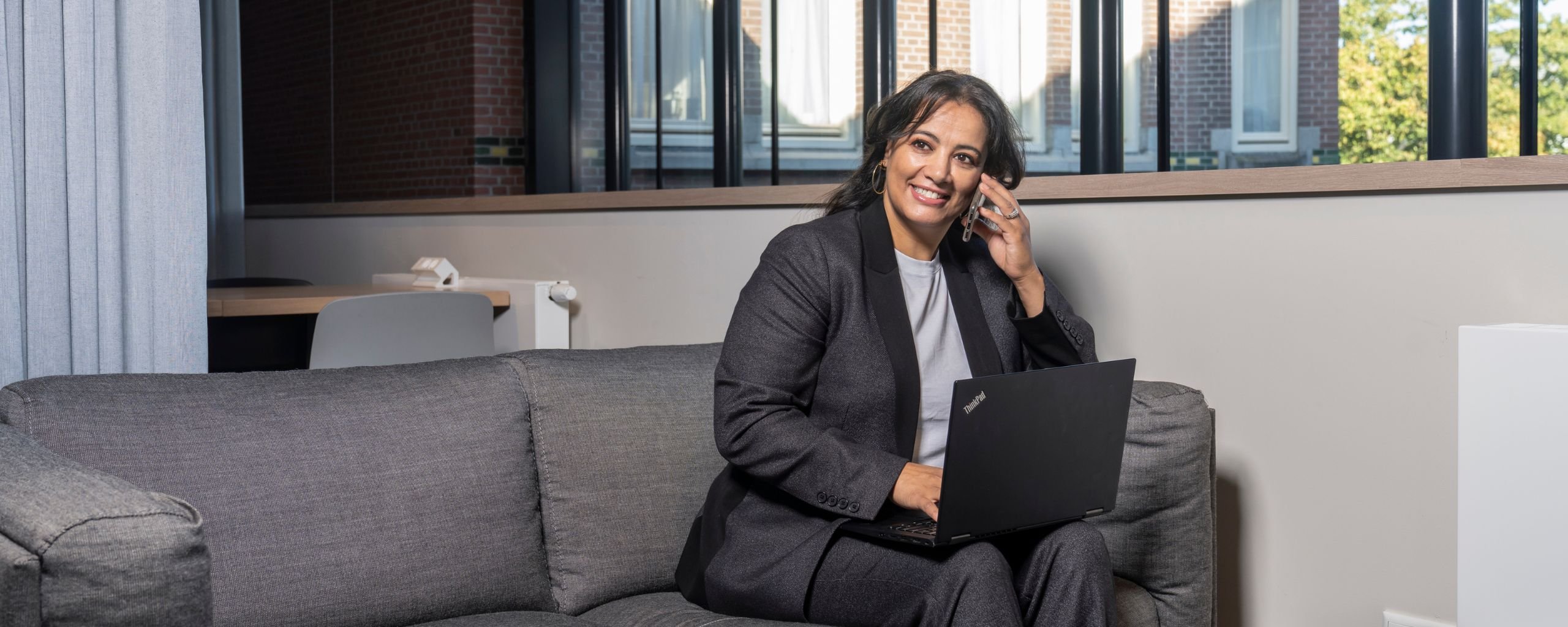 Een medewerker voert een telefoongesprek in de ontmoetingsruimte, waar ze aan het werk is achter de laptop.