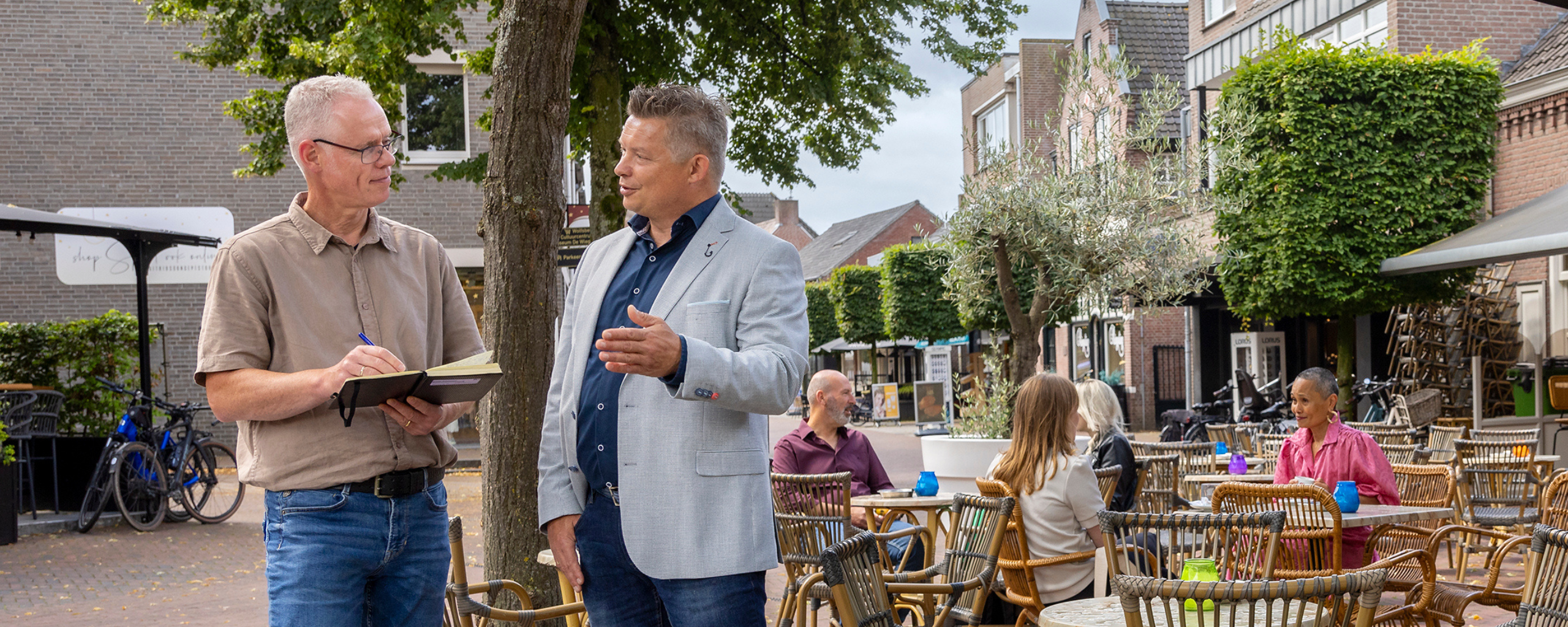 De twee personen zijn met elkaar in gesprek, ondertussen maakt de linker medewerker notities van het gesprek.
