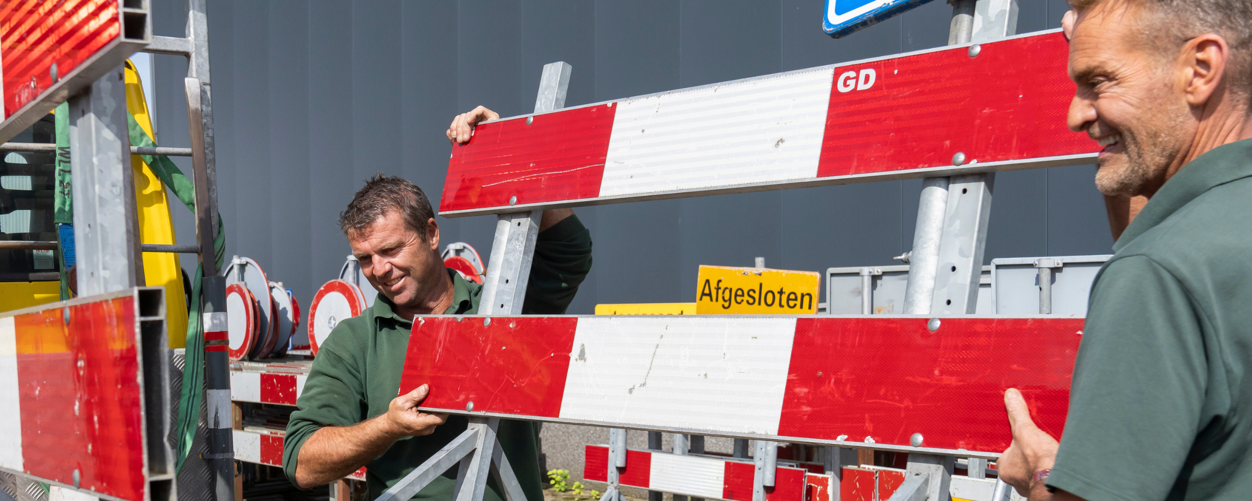 Twee collega’s van de buitendienst tillen een omleidingsbord op de aanhangwagen.