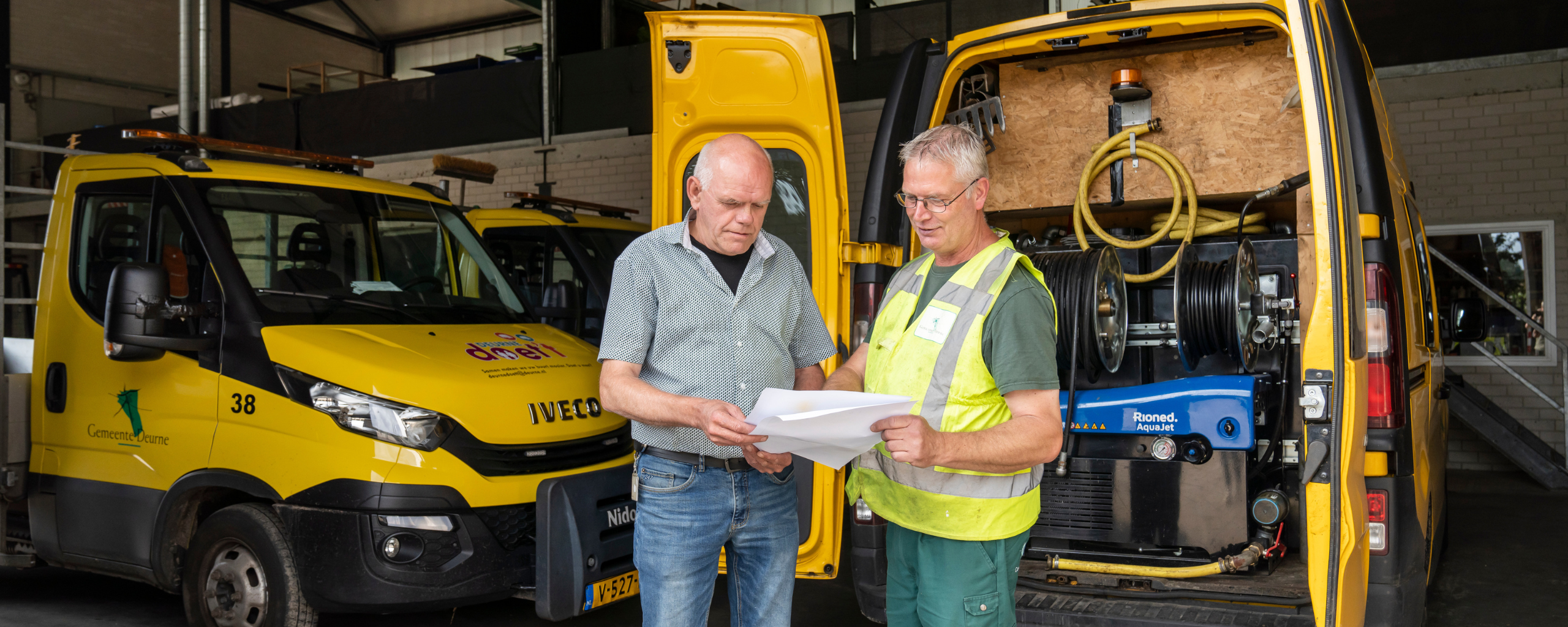 Twee buitendienst medewerkers bespreken samen wat er op het papier geschreven of afgebeeld staat.