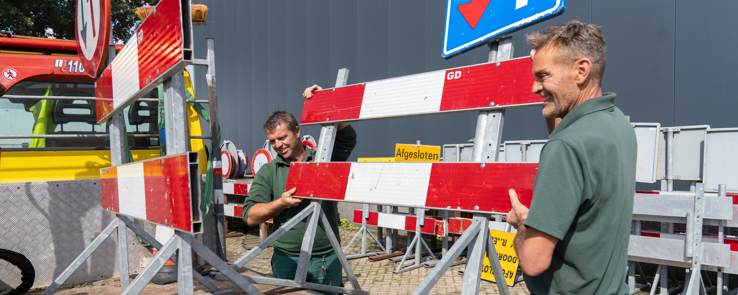 Twee collega’s van de buitendienst tillen een omleidingsbord op de aanhangwagen.