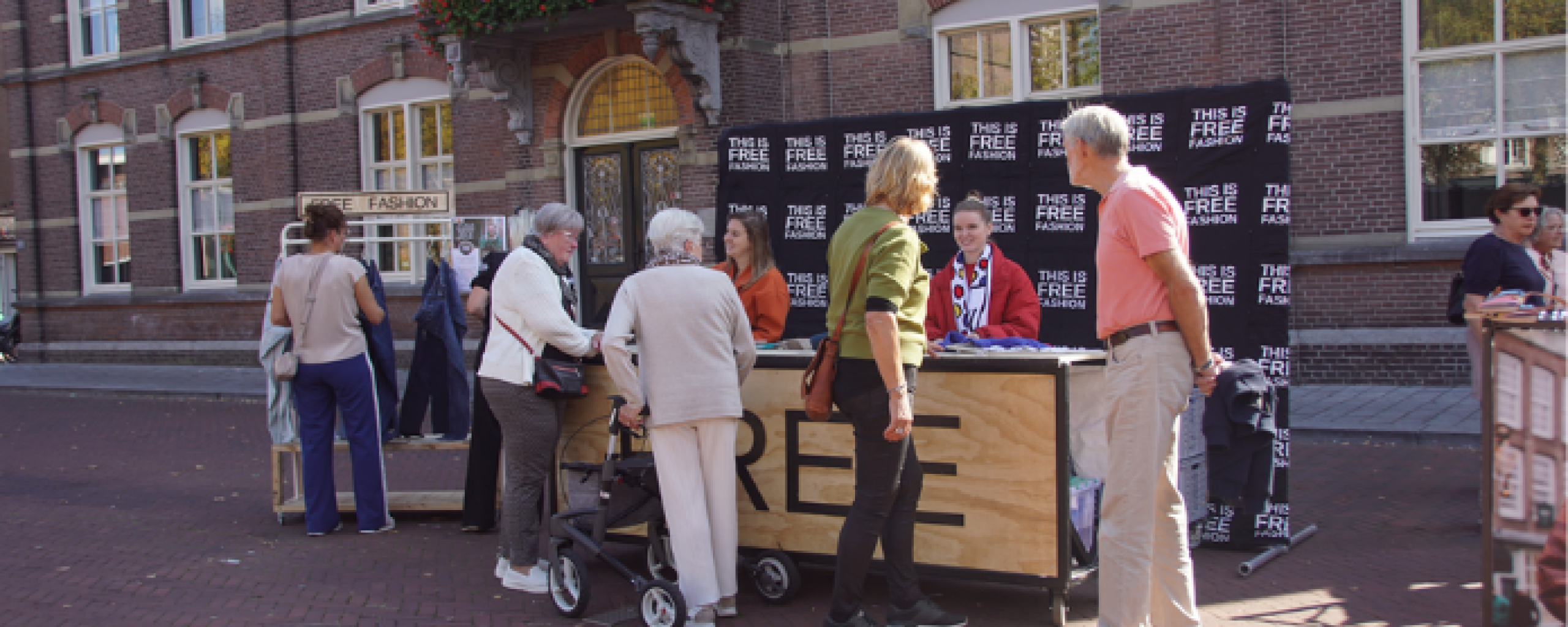 Bezoekers van de Free Fashion Kledingkar op de Markt in Deurne bekijken kleding