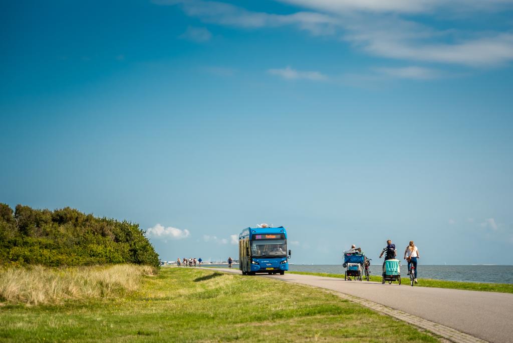 Elektrische Arriva bus op Vlieland over weg langs water met fietsers en blauwe lucht