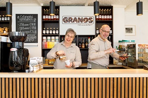 Eigenaren Granos koffiebar man en vrouw staand lachend achter toonbank met accessoires