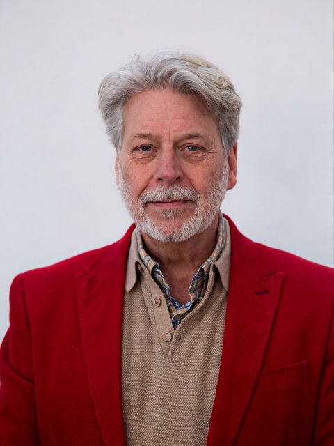 Profielfoto man middelbare leeftijd, grijs baardje, overhemd met beige sweater en rode pakjas