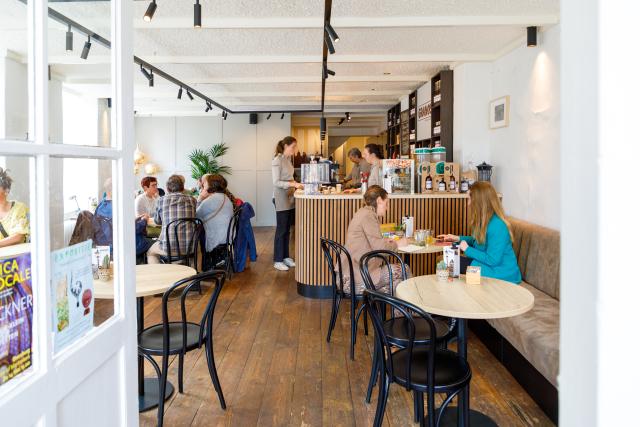 Interieur Granos koffiebar met zittende mensen aan ronde tafels