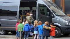 Jonge schoolkinderen staan te wachten voor en stappen in de geopende taxibus