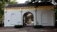Rechthoekig wit gebouw met middenin ovaal poortje en herkwerkje als toegang naar begraafplaats