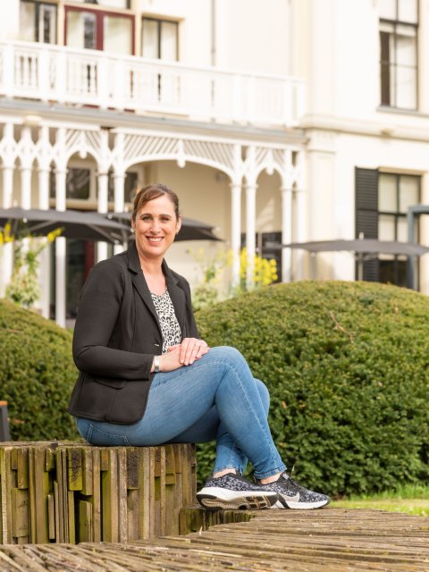 Audrey zit op een stenen trap voor een groene heg. Op de achtergrond staat hotel Ruimzicht