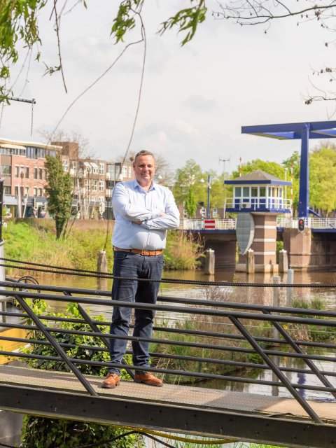 Gerben staat op een loopbrug voor het water. Op de achtergrond een ophaalbrug met een wachtershuisje. Aan de overkant van het water staan enkele appartementen.