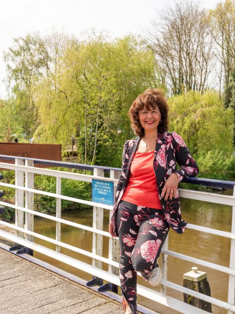 Maureen staat tegen de railing van de fietsbrug. Met één been op de brug.