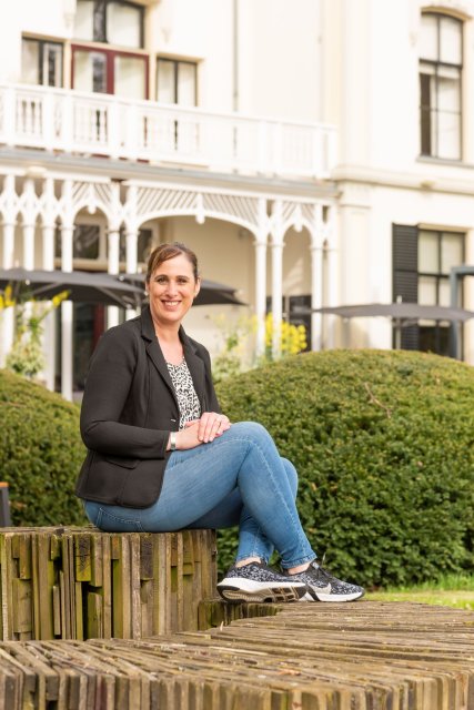 Audrey zit op een stenen trap voor een groene heg. Op de achtergrond staat hotel Ruimzicht