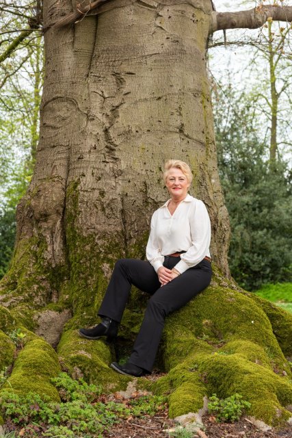 Georgette zit op de wortel van een ontzettend grote boom. Alleen de dikke stam is zichtbaar.  De wortels zijn begroeid met mos.