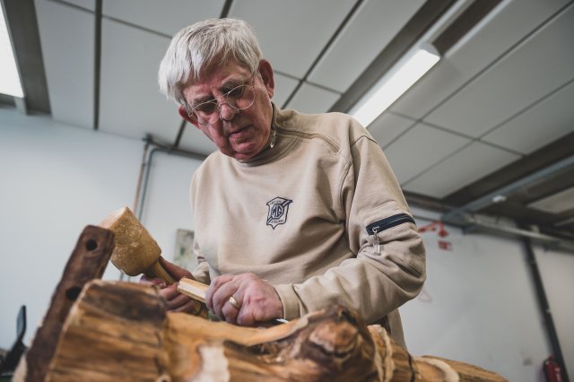 Een man in een stuk hout aan het bewerken met een beitel en een houten hamer.