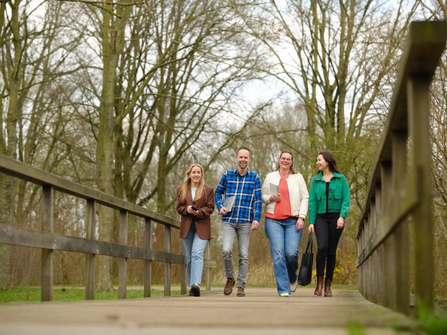4 Wandelaars op een houten brug. Op de achtergrond bomen.