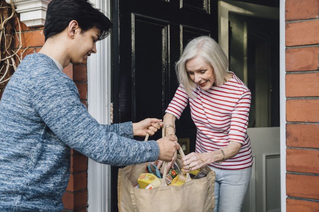 Jongen geeft boodschappentas met boodschappen aan oudere vrouw.