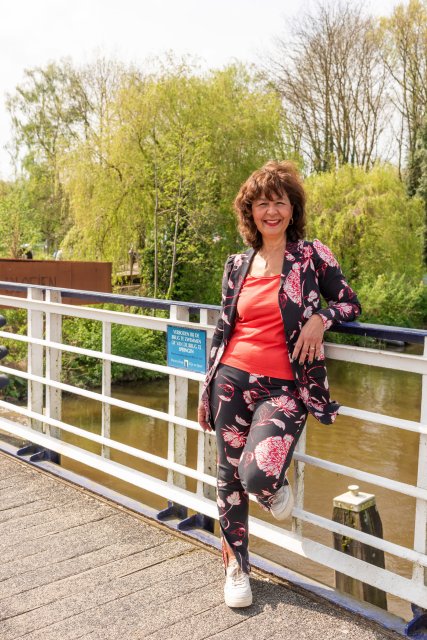 Maureen staat tegen de railing van de fietsbrug. Met één been op de brug.