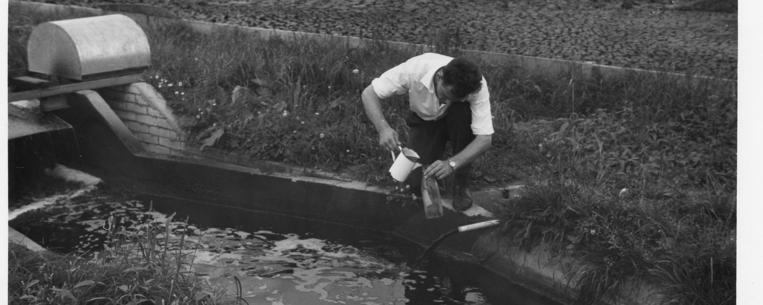 Een oude zwart wit foto van een man die een monster neemt uit een sloot op de eerste proefzuivering in Eersel.