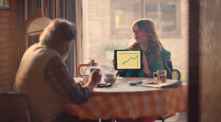 Jonge vrouw toont aan tafel een grafiek op een tablet aan een seniore man