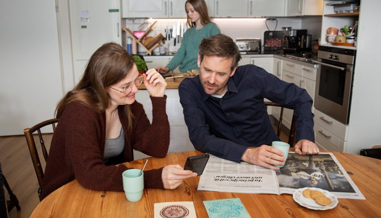 Vrouw toont aan de keukentafel iets op haar mobiel aan haar man