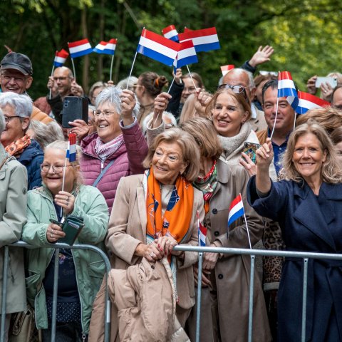 Vele toeschouwers zwaaien lachend met Nederlandse vlaggetjes