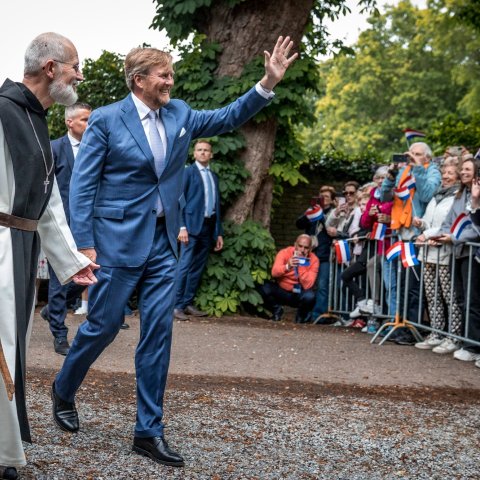 Koning Willem Alexander zwaait naar het publiek in het bijzijn van een monnik