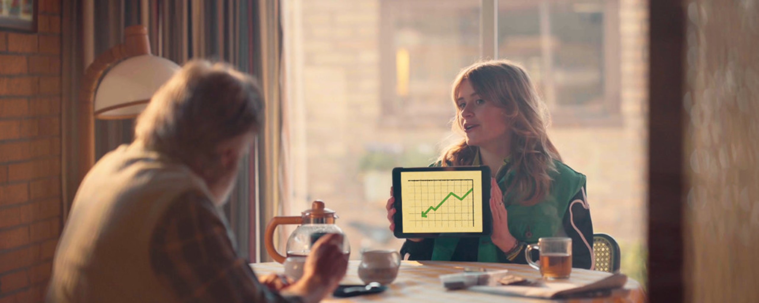 Jonge vrouw toont aan tafel een grafiek op een tablet aan een seniore man