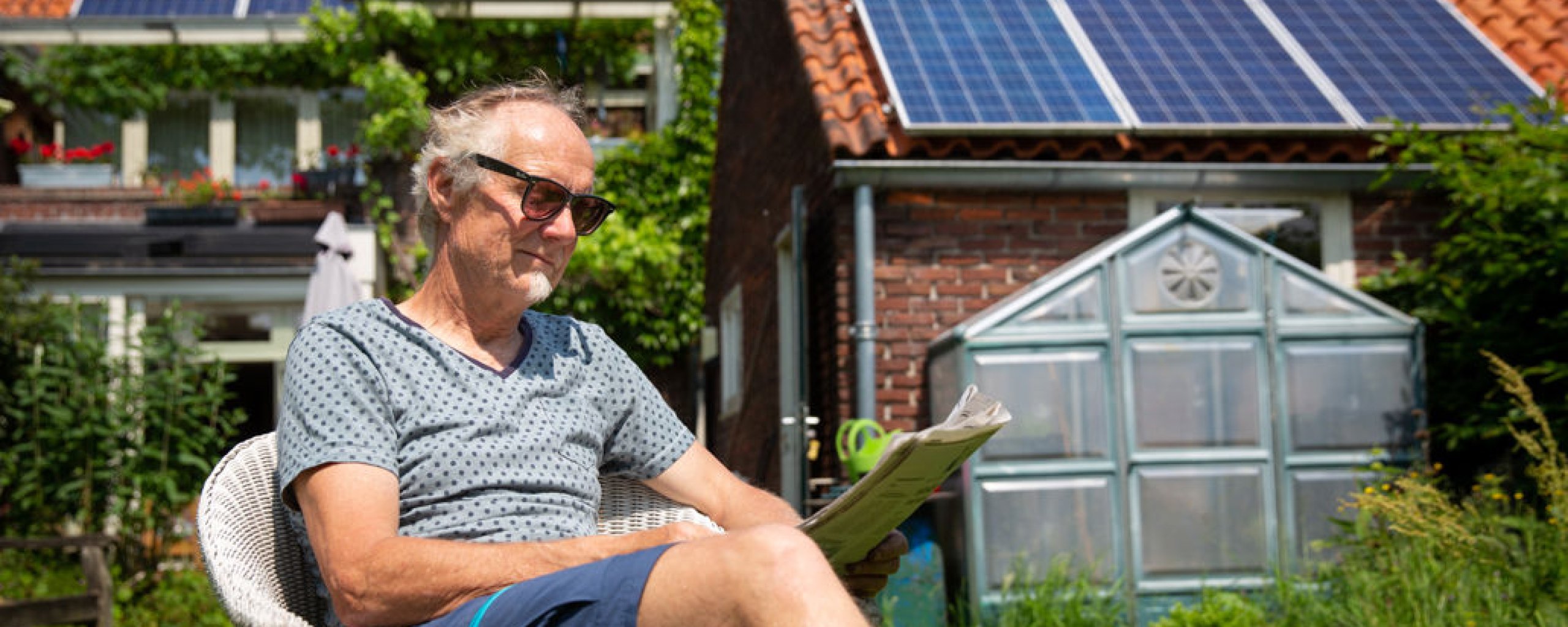 Man zit in zijn tuin in de zon de krant te lezen