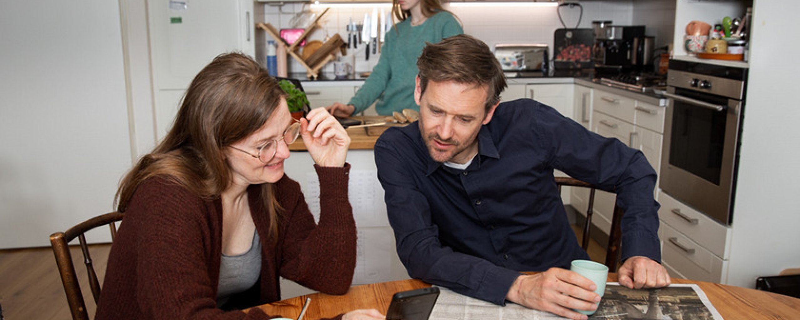 Vrouw toont aan de keukentafel iets op haar mobiel aan haar man